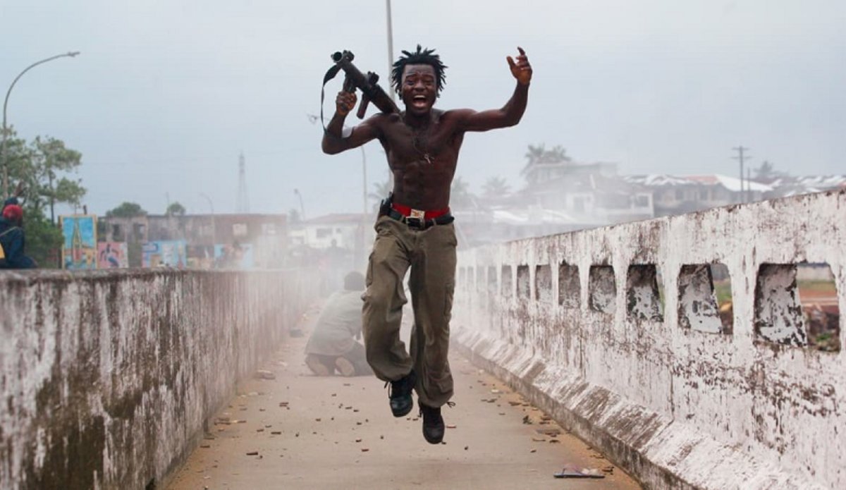 Командир группы либерийских ополченцев торжествует, запустив реактивную гранату по силам повстанцев на стратегически важном мосту в Монровии, 20 июля 2003 года. Фото: Крис Ондрос